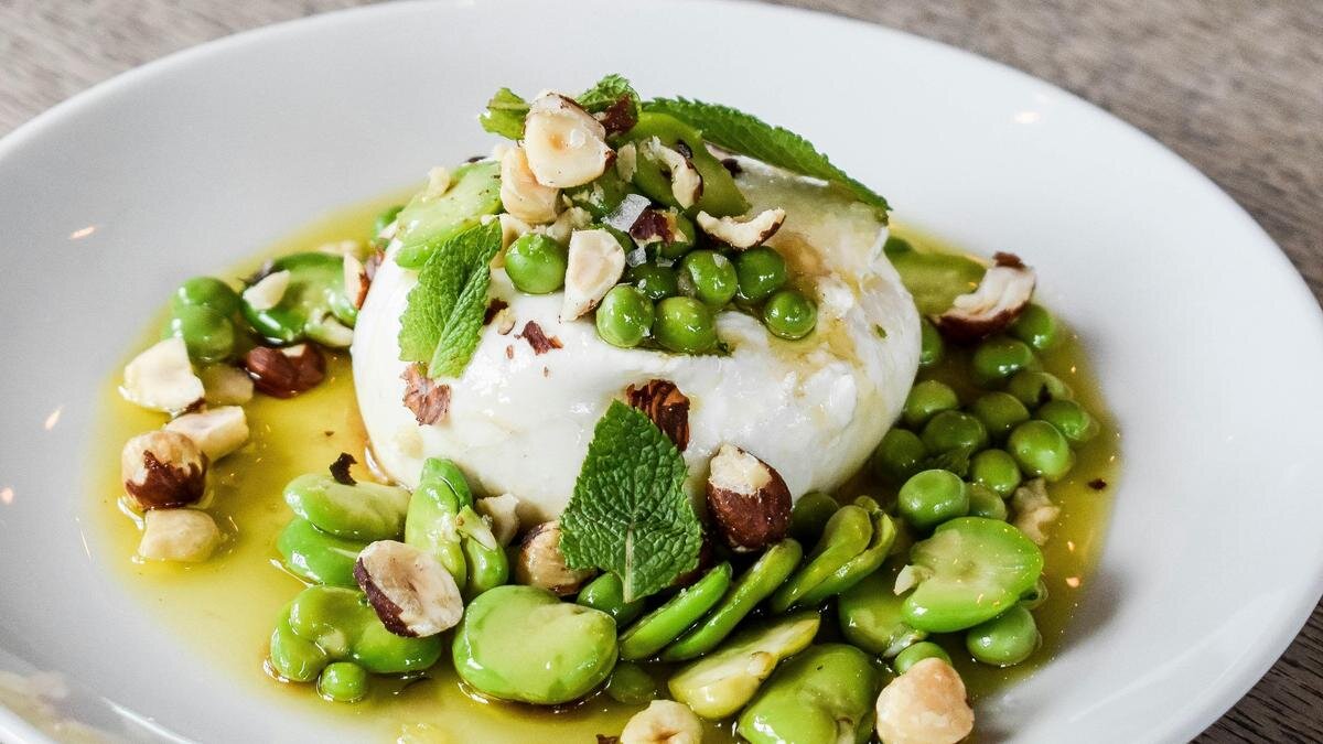    На сервировочной тарелке сыр буррата с зеленым горошком, орехами и мятой в соусе:Unsplash/ Amy Vann