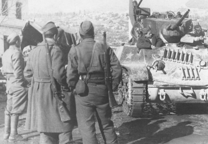 На этом снимке солдаты 1-й бригады Народно-Освободительной Армии Югославии и танк М5 «Стюарт» американского производства на улице югославского городка Широки Бриег, ныне территория Боснии и Герцеговины. У бойца на переднем плане слева - трофейная немецкая 7,92-мм винтовка Маузер образца 1898 года. Солдат справа вооружен трофейным итальянским 6,5-мм карабином Moschetto per Cavalleria M1891.