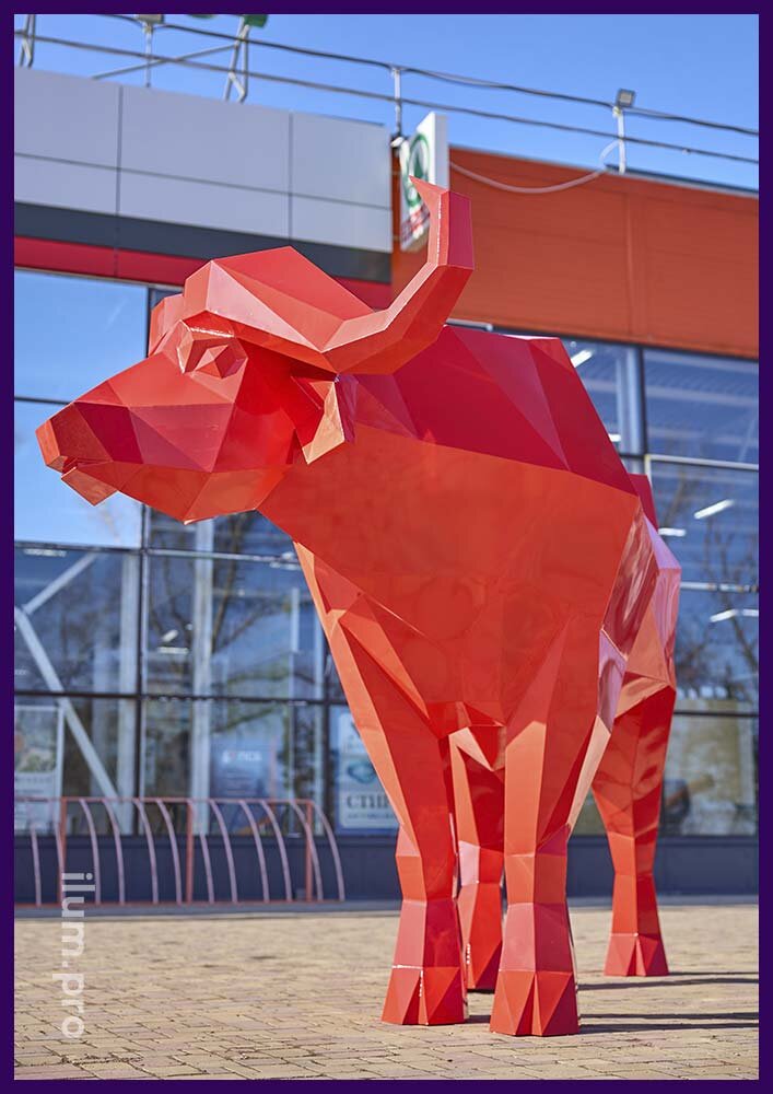 Полигональная скульптура большого, красного буйвола на парковке торгового центра