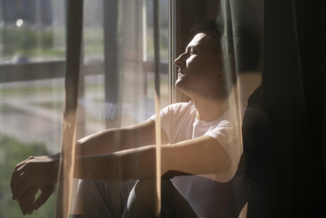    Задумчивый мужчина сидит на окне и смотрит наружу:Freepik