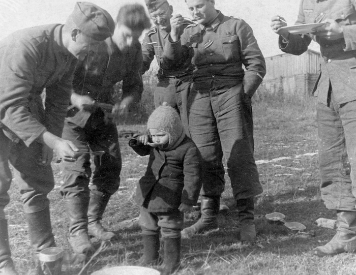 Немецкие солдаты едят кашу и кормят ей советского ребенка. Фото для иллюстрации