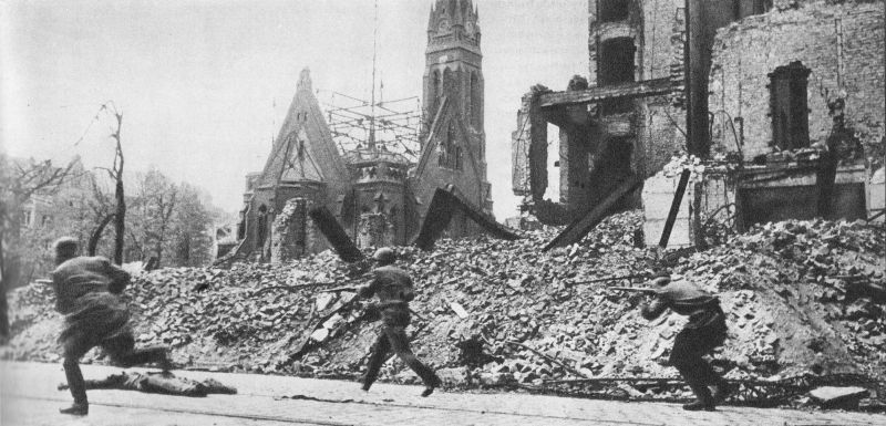 Красноармейцы бегут мимо разрушенной церкви на улице Берлина.