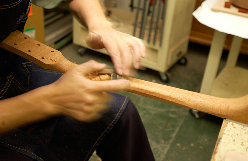 Лютье формирует изгиб грифа рубанком