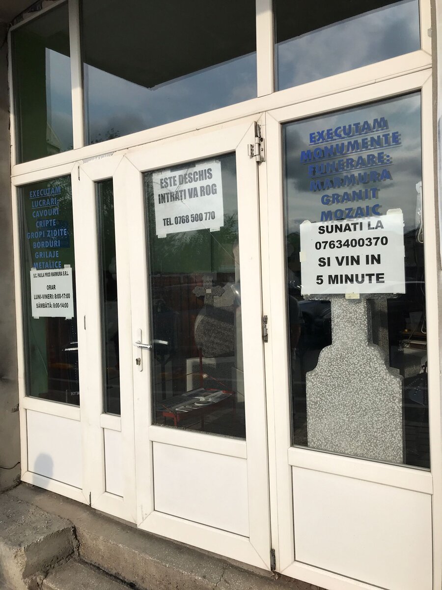 Рядом с булочкой можно прикупить камешек. На объявлении написан номер телефона — позвони и хозяин придет через 5 минут. Лавка ритуальных памятников на площади у вокзала, город Джурджу, Румыния, 2024 г.