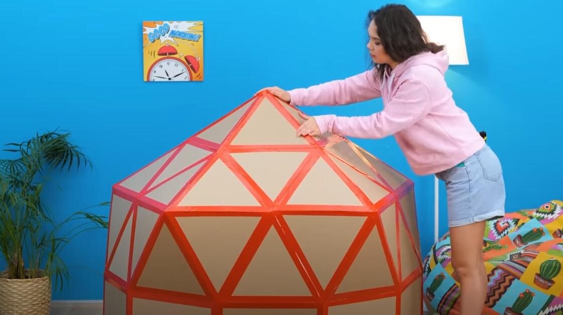    Девушка приклеивает скотчем крышу на картонном домике:YouTube/БЕРИ И ДЕЛАЙ