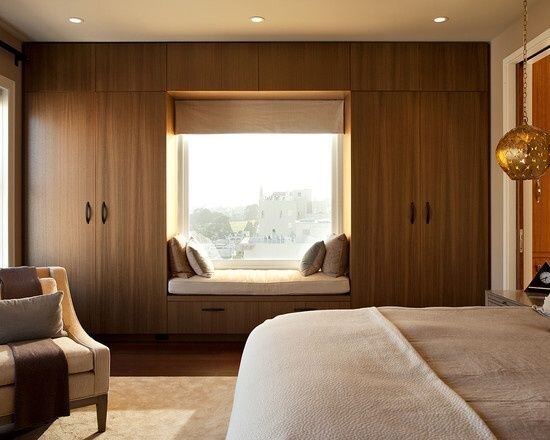 Классический вариант шкафа вокруг окна: встроенная конструкция с антресолью и подоконником-скамьей.  