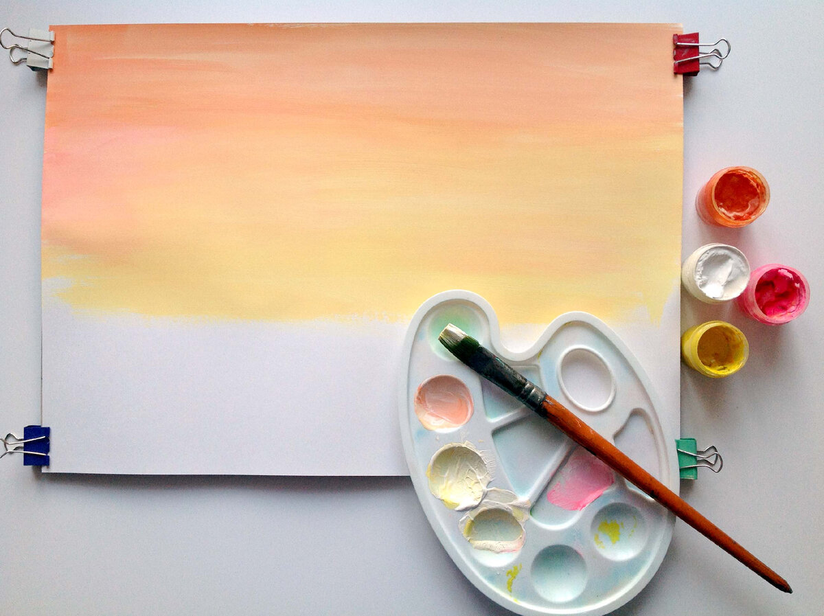 Рисуем раннее утро, выбираем  теплые цвета для неба. Можно придумать свой рассвет, свою теплую цветовую гамму. Возможно, вам захочется уйти в более розовую гамму, красную, оранжевую или желтую.  Можно сделать цветовую растяжку от более насыщенного тона  к более светлому . Кистью большого размера быстро закрываем лист бумаги краской. Пока краска не высохла легко добиться плавных цветовых переходов. Чтобы небо зрительно не перебивало по яркости сам рисунок, сделаем его  пастельных цветов, добавляя в основные выбранные цвета белую краску.