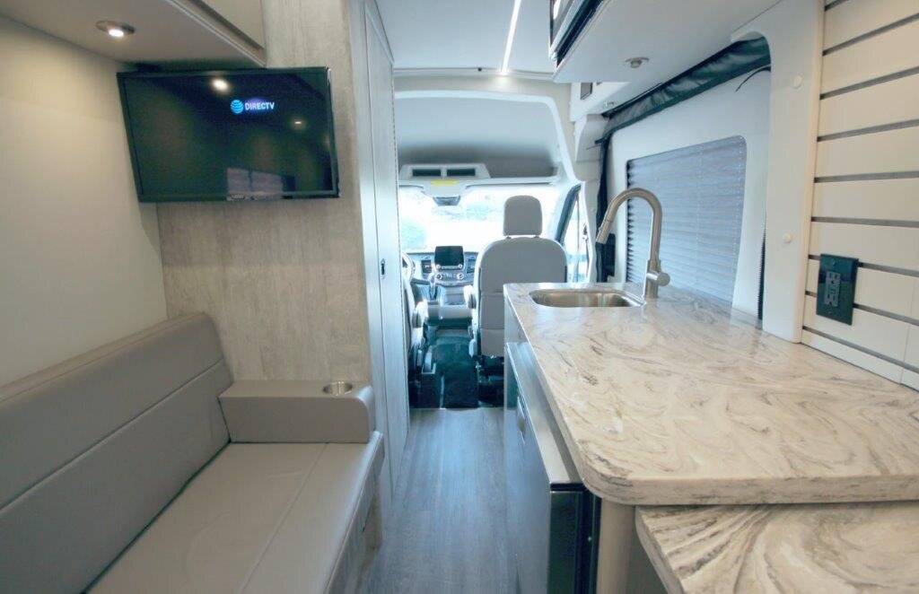 Обеденная и кухонная зона расположены в средней части, что отличается от классического решения делать его в передней зоне, сразу за водителем. Как по мне это не очень удобное решение. Мини-кухня с раковиной, микроволновой печью, холодильником/морозильником с большим выдвижным ящиком и двумя откидными столиками/удлинителями стойки.