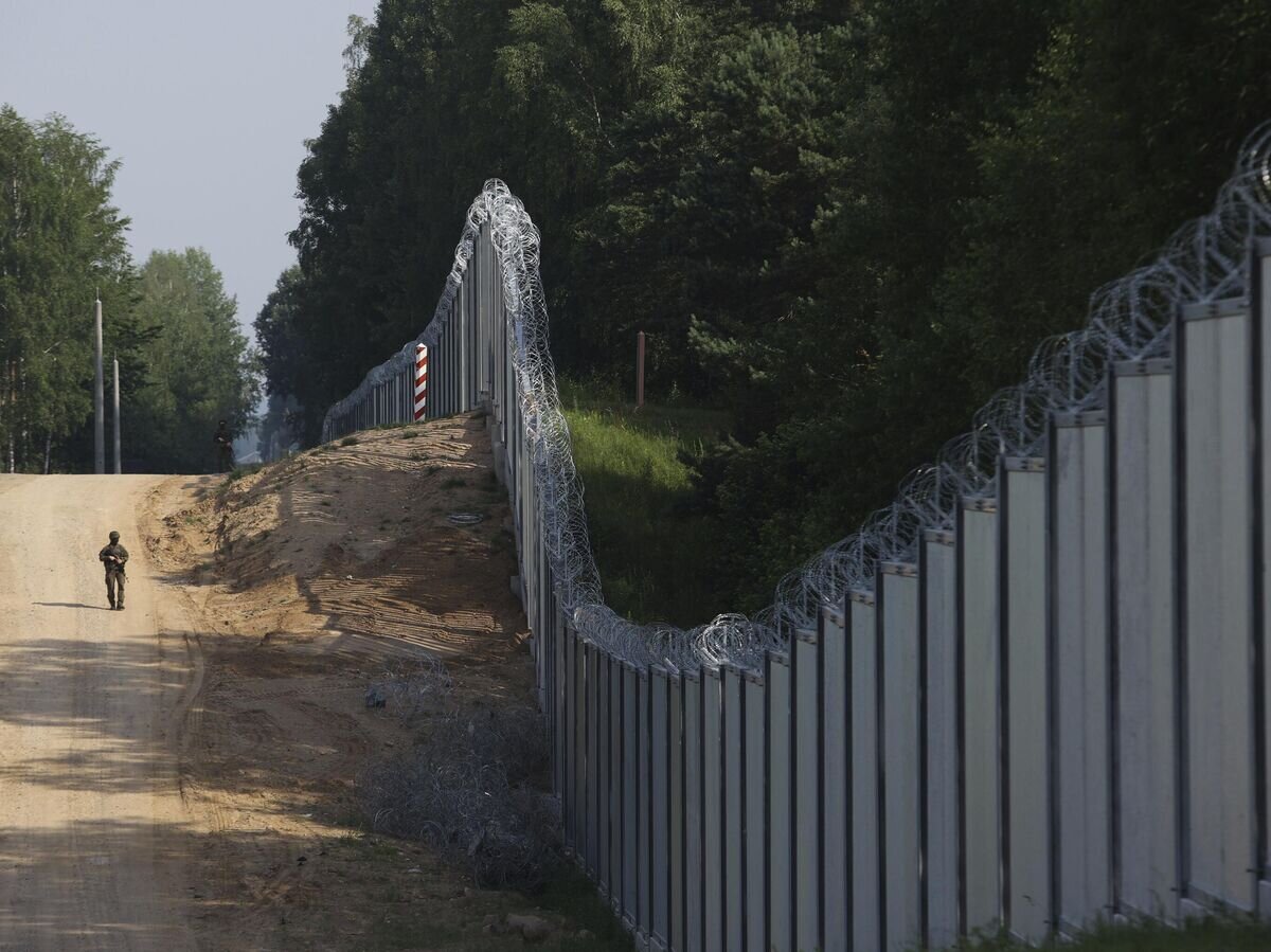    Польский пограничник идет вдоль металлического забора на границе Польши и Белоруссии© AP Photo / Michal Dyjuk