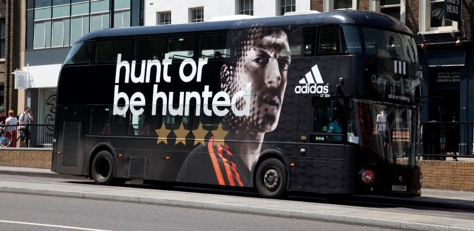 Эта наружная реклама Adidas эффективно привлекает внимание благодаря впечатляющему и яркому изображению спортсмена и лозунгу "hunt or be hunted", что мгновенно создает сильный, динамичный образ, способствующий узнаваемости бренда. 