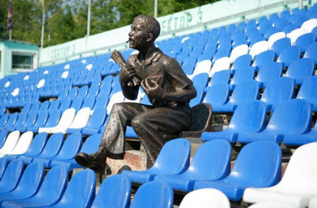 Памятник болельщику  на скамейке стадиона «Труд» в Томске, в руке у него газета «Футбол-Хоккей».