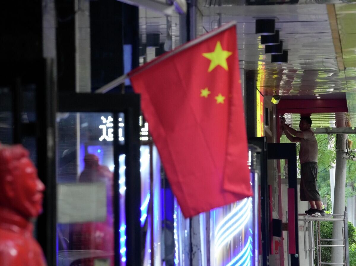    Рабочий возле национального флага в Китае© AP Photo / Ng Han Guan