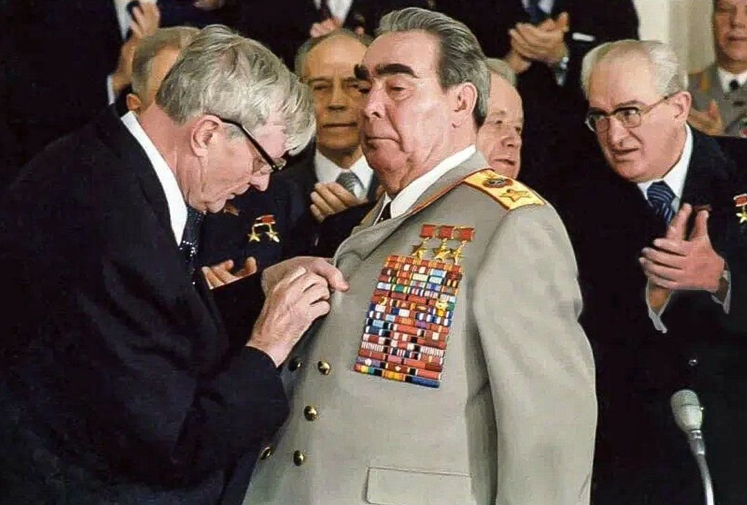 Михаил Андреевич Суслов пытается проколоть дырку на пиджаке Брежнева для ордена "Победа"