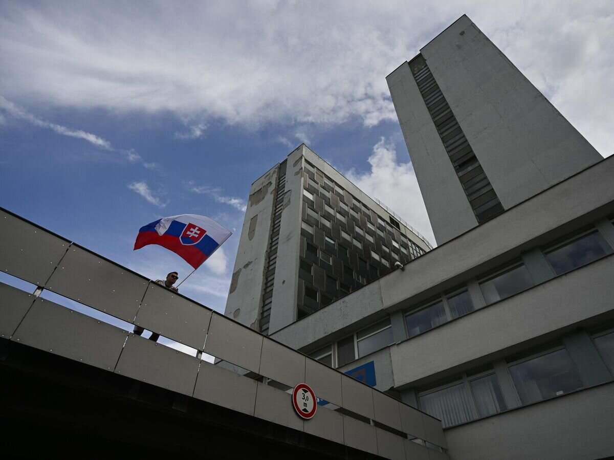    Мужчина с флагом Словакии у здания университетской больницы имени Ф. Д. Рузвельта, где проходит лечение раненый премьер-министр Роберт Фицо, в Банска-Бистрице© AP Photo / Denes Erdos