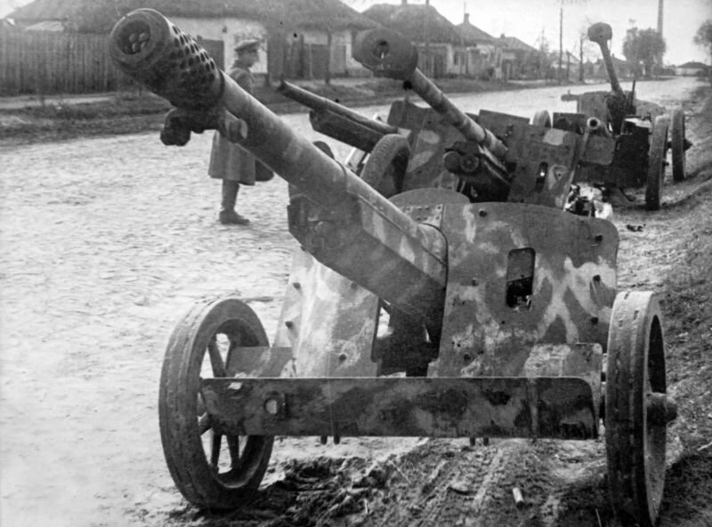 Брошенные немецкие противотанковые пушки PaK 97/38 (7,5 cm schwere Panzerjägerkanone 97/38 L/36,3) и PaK 36(r) (7,62 cm Panzerjägerkanone 36(r) — глубокая модернизация советской дивизионной пушки Ф-22) на улице освобожденного советского села.
