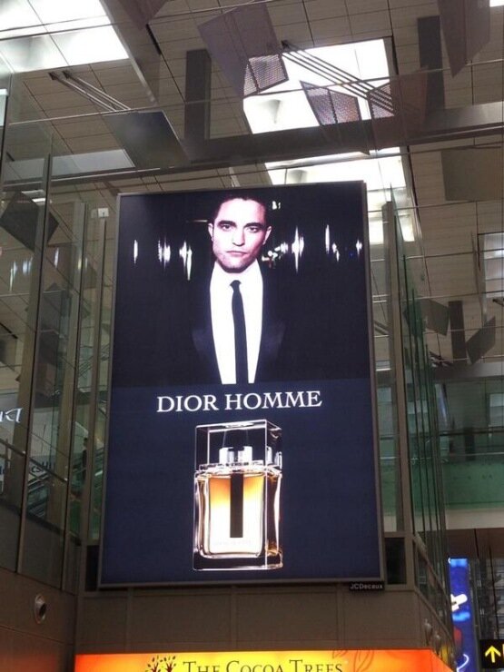 Эта наружная реклама Dior эффективно привлекает внимание, сочетая элегантный образ мужчины в классическом костюме с изображением флакона парфюма Dior Homme. 