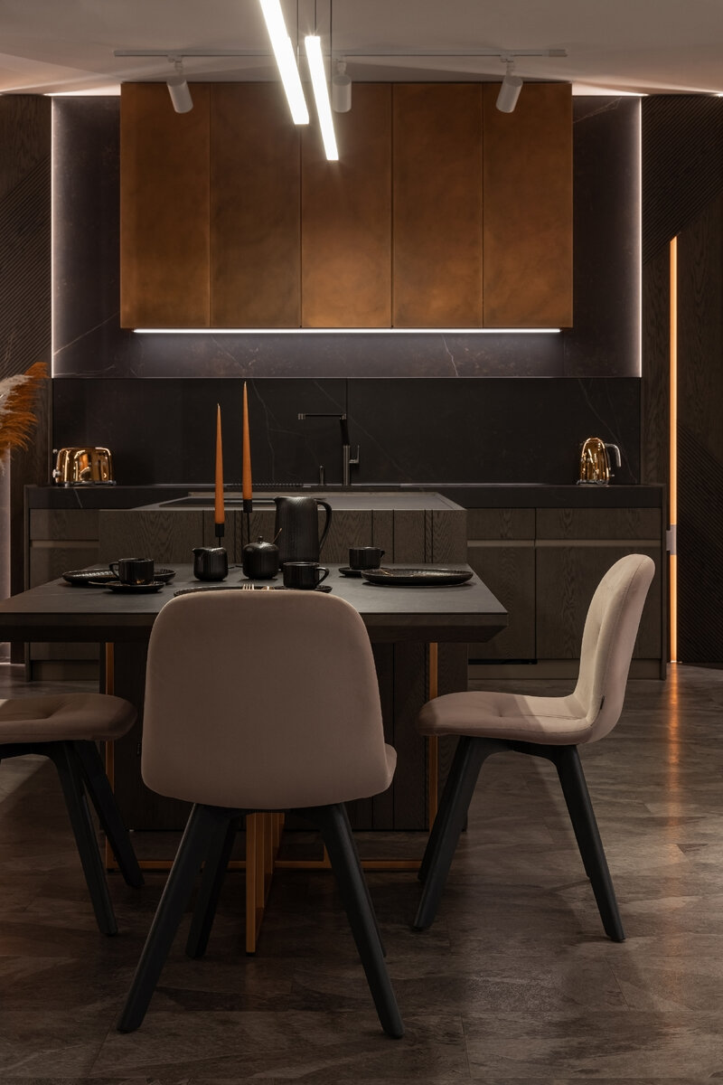 Дополняет композицию приставной обеденный стол в оригинальным подстольем в отделке эмалью со спецэффектом под медь. Столешница со скошенным краем выполнена из тех же материалов, что и кухня: шпон Дуб Vintage Grey и керамический камень Dekton.