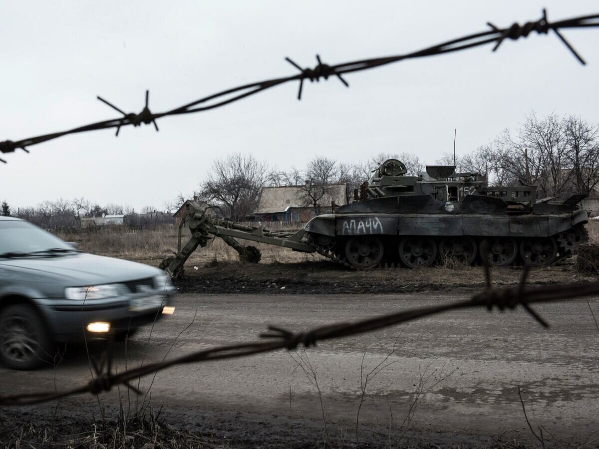    Автомобиль проезжает мимо брошенного танка украинской армии в Очеретино© AP Photo / Evgeniy Maloletka
