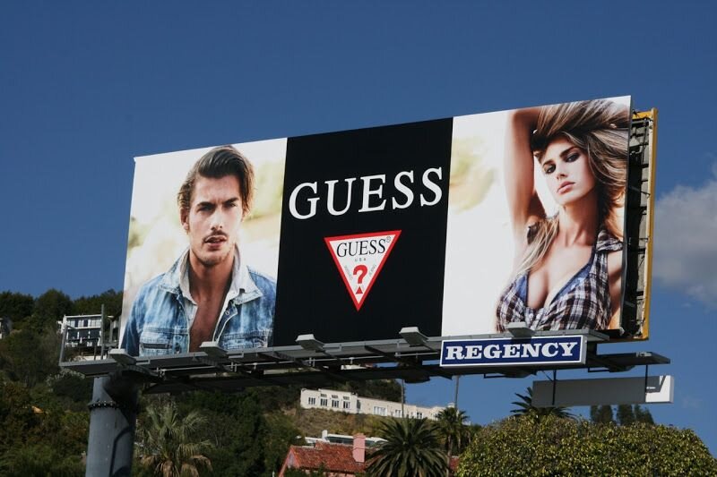 Эта наружная реклама магазина одежды Guess эффективно привлекает внимание стильными изображениями моделей и узнаваемым логотипом бренда. 