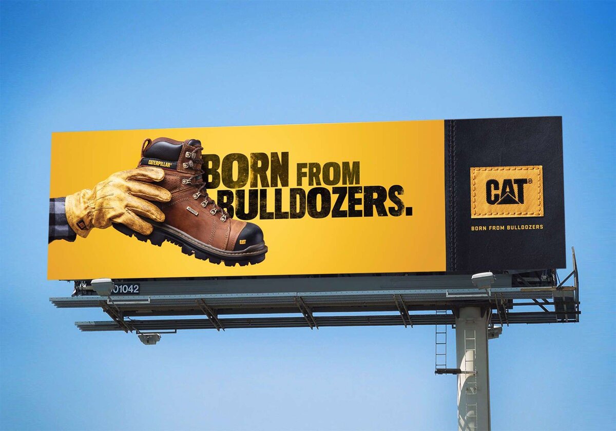 Реклама обуви CAT демонстрирует ботинки, подчеркнутые слоганом "Born from Bulldozers," на ярком желтом фоне с логотипом бренда. 