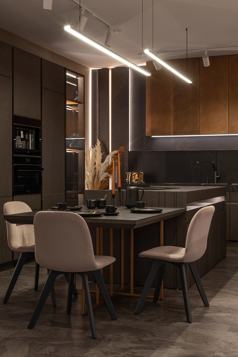 Первое впечатление производит сочетание материалов в теплых оттенках и игра объемов, изысканно подчеркнутых дополнительной встроенной подсветкой. Дизайнеры салона сделали ставку на комбинацию темного шпона Дуба серии Vintage, натуральной меди, керамического камня Dekton и стекла с зеркальным напылением.