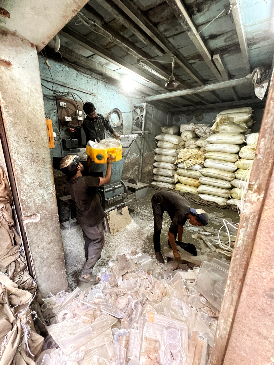 Мужчины закидывают пластик в машину, которая его перемалывает.