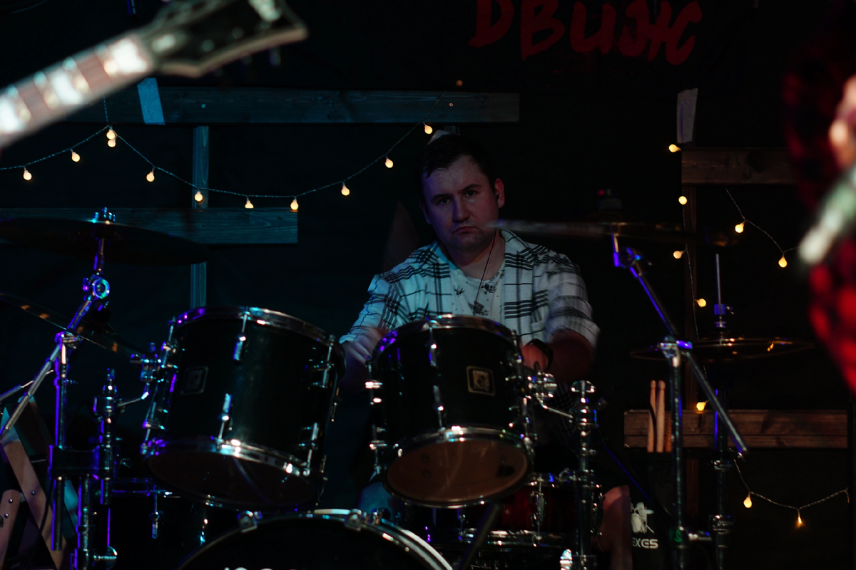 Дербенев Сергей в раннем детстве хотел играть на барабанах, но к великому счастью его соседей, барабаны не купили. Против гитары никто ничего не имел, и с третьего класса по разным самоучителям он начал познавать прелести трех аккордов. Следующим этапом было получение от знакомого сестры, повидавшую виды бас-гитару 🎸 Jolana Galaxis Bass, которую дали на восстановление и благополучно забыли про нее. С ее помощью с 2006 года Сергей начал играть панк-рок с разными коллективами на различных площадках типа «приведи 5 друзей и сыграй с десятью другими командами, никак не связанными между собой по стилям». В результате в роли басиста Сергей пришёл в East F.A.Q., но мечты должны сбываться, и осенью 2023 года, после ухода барабанщика 🥁, он решил попробовать себя в новой роли.