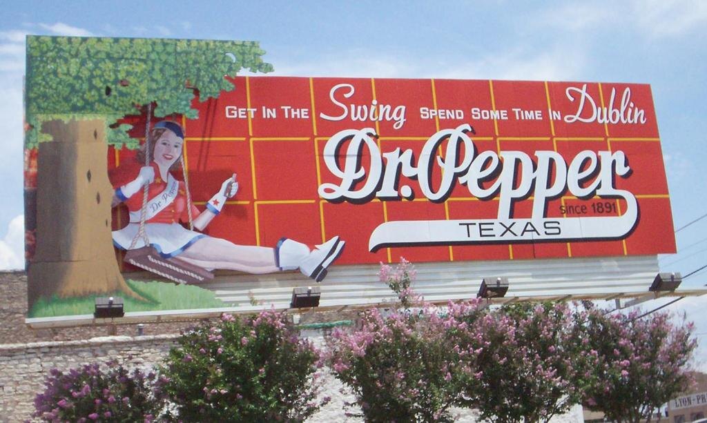 На этом креативном билборде Dr Pepper изображена девушка, сидящая на качелях под деревом, с надписью "Get in the Swing, Spend Some Time in Dublin" и логотипом Dr Pepper, рекламирующим напиток в Техасе с 1891 года. 