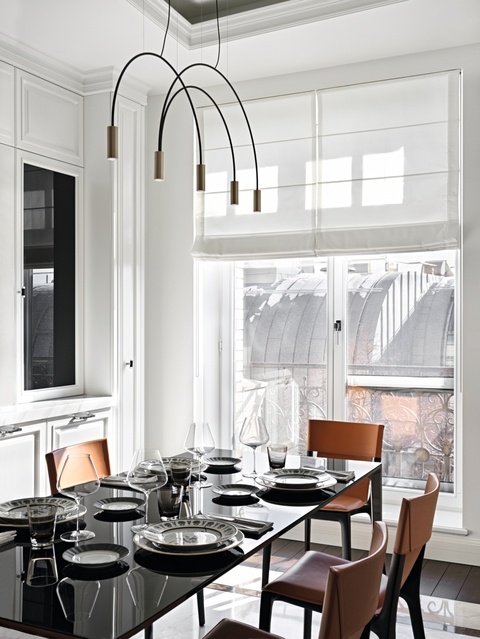 Кухня с обеденной зоной отделена от гостиной распашными стеклянными дверями. Стол с черной стеклянной столешницей Rimadesio дополняют стулья Poltrona Frau, обтянутые натуральной кожей ярко-рыжего цвета. Кожаные ручки кухонных шкафов, Turnstyle Designs. Над обеденным столом — подвесной светильник Volta, Estiluz. Тарелки, Richard Ginori.