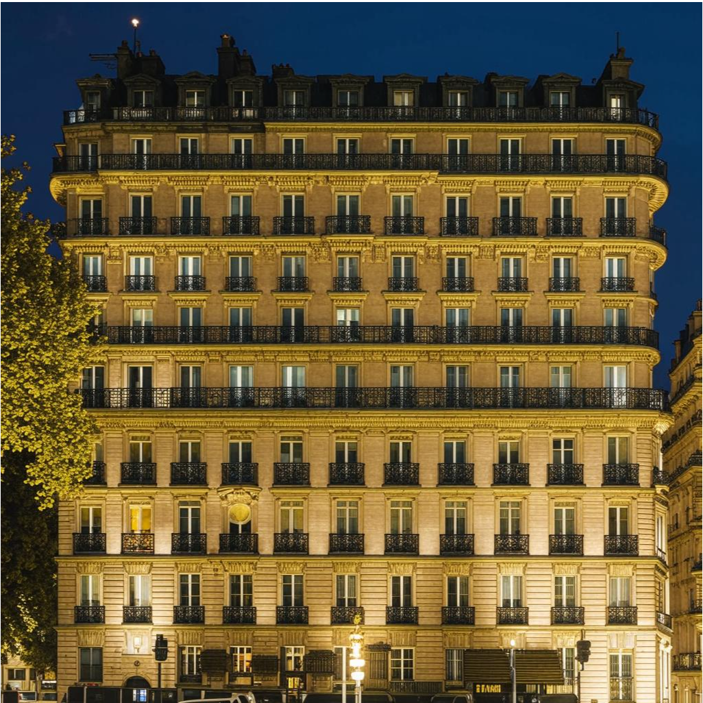 Роскошный отель The Ritz-Carlton в центре Парижа, элегантные фасады, окруженные зеленью, ночное освещение, подчеркивающее архитектурные детали.