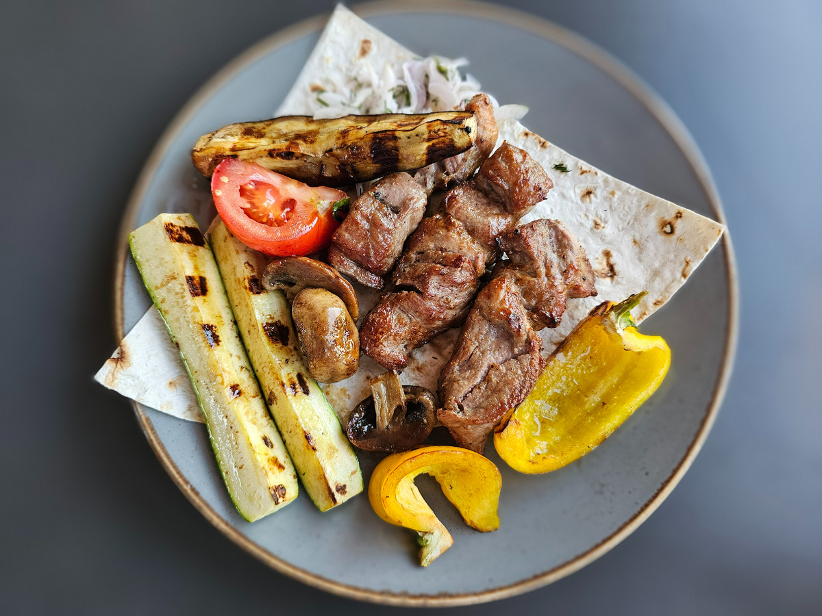 На фото — мой ранний ужин в Крыму, состоящий из свиного шашлыка, обжаренных овощей (перца, помидоров, кабачков, баклажанов) и грибов. Всё это подаётся на лаваше. Красное мясо я ем не чаще 2–3 раз в неделю и не более 200 г на порцию. По мнению нейросети, это блюдо может быть частью здорового рациона. А что думаешь ты?