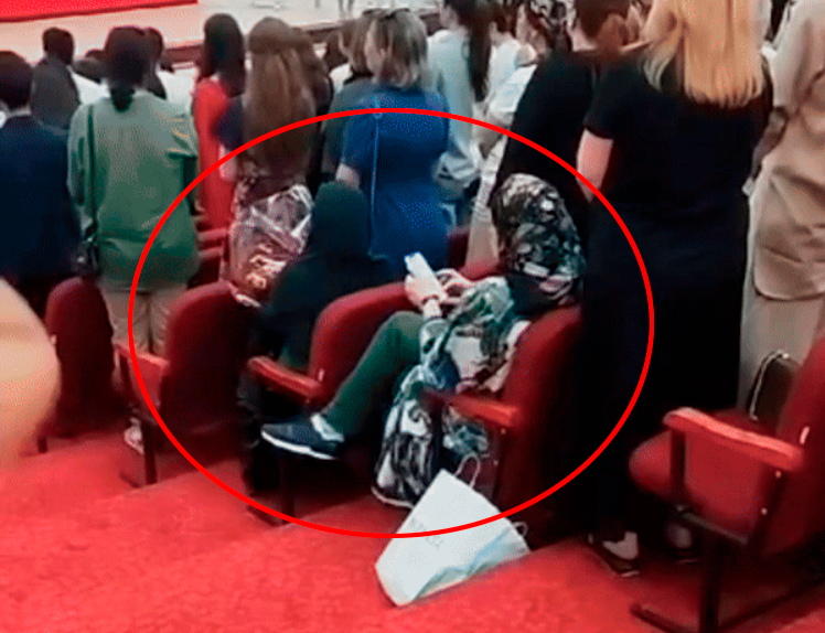 Все встали, а мамы в хиджабах продолжили зависать в телефонах. Фото: скрин видео.    