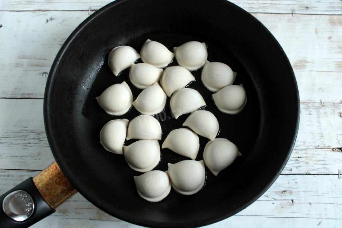 Пельмени выньте из морозилки и сразу переходите к их жарке. Размораживать пельмени не нужно, иначе они станут прилипать к сковороде, тесто порвется, а мясной сок вытечет из начинки. В толстостенную сковороду налейте растительное масло, хорошо разогрейте его. Выложите в сковороду пельмени. Важно, чтобы пельмени лежали в один слой, не касались друг друга «ушками» и не слипались между собой.