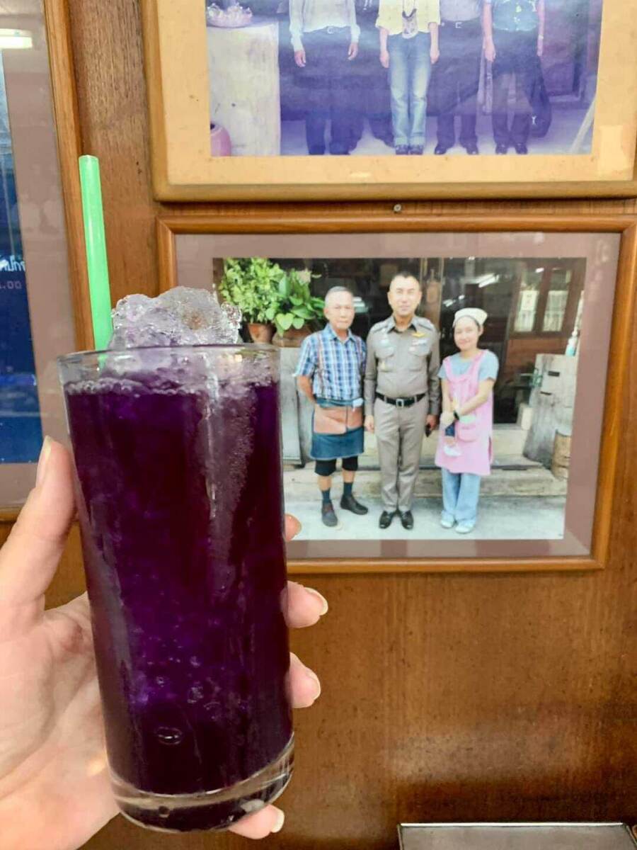 Стакан напитка насыщенного филотеового цвета со льдом  на фоне портрета Генерала  полиции в тайской едальне.  Фото Марины Поарн. 