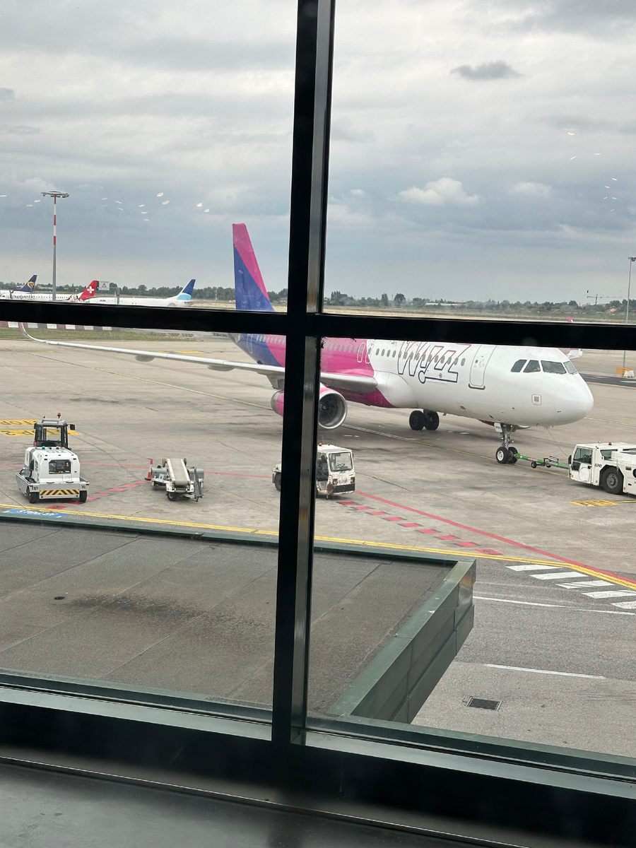 Wizz Air A320-232 в Яссы, Румыния. Очень много галдящих пассажиров несущих вещи в полиэтиленовых пакетах и тканевых сумках. Атмосфера рейсов между некрупными городами России. На фоне видно Embraer “Helectric” в Цюрих, Швейцария и Boeing 737-800 “Ryanair” куда-то, ещё видно Boeing 737-300 “ASL  Airlines Cargo