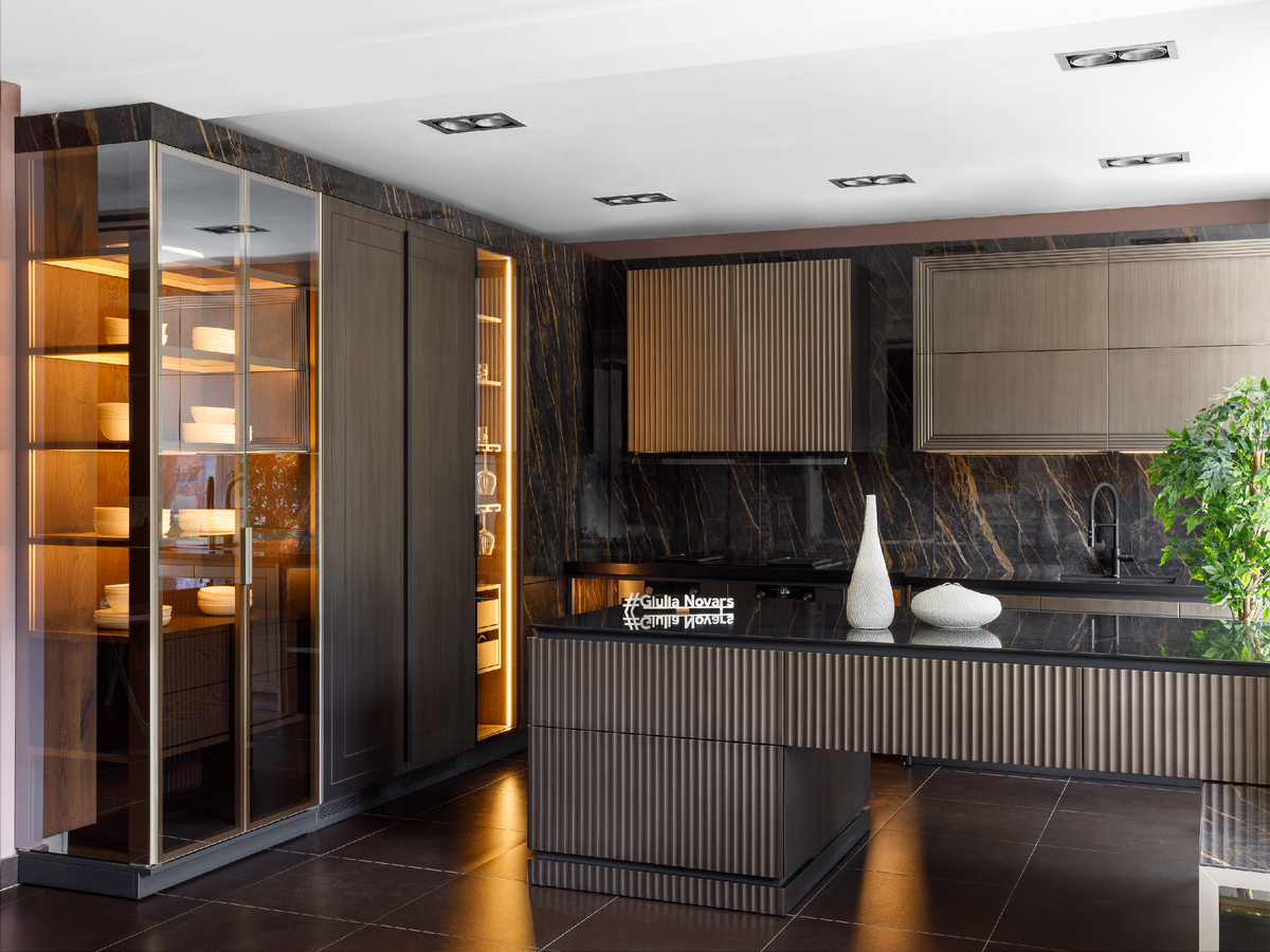 Притягивают внимание и задают характер темные оттенки эмали под бронзу, керамики с рисунком под мрамор, шпона Дуба в винтажной отделке в сочетании со стеклом и стальными конструкциями. Декоративная подсветка подчеркивает игру объемов, а также внутреннее наполнение витрин, тем самым дополняя разноуровневый сценарий освещения помещения в целом.