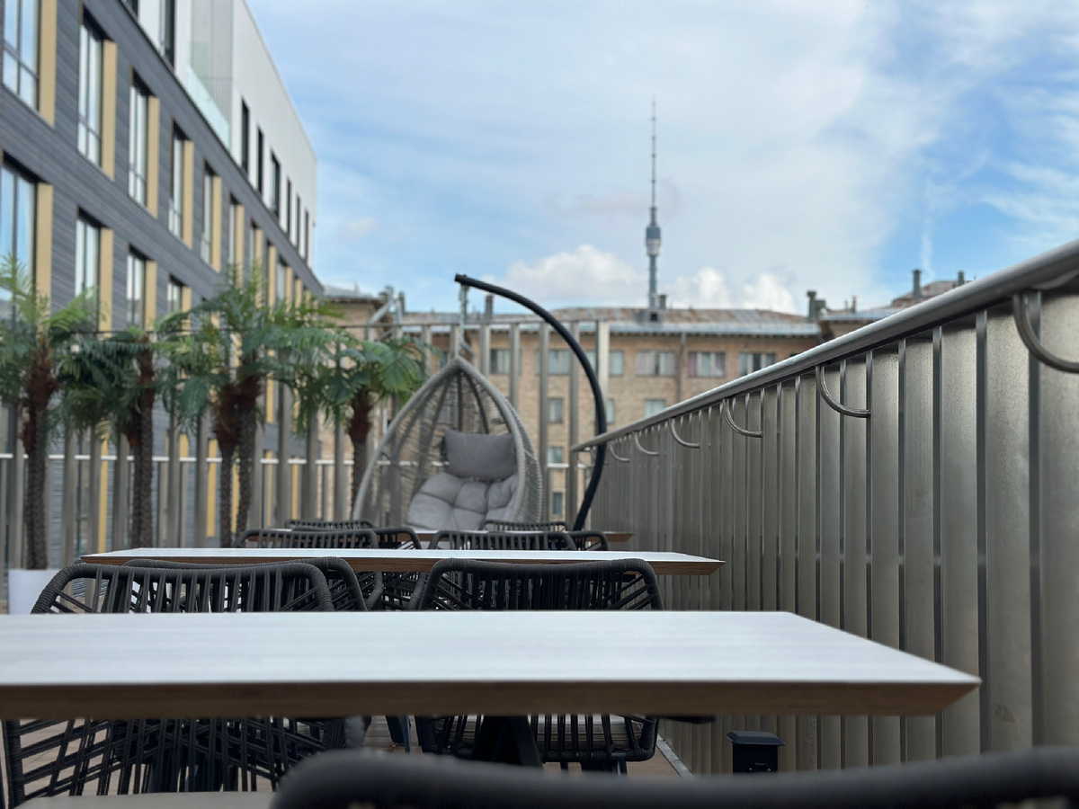 Открытая часть второго уровня. Два круглых кресла напротив друг друга, вид на Останкинскую башню, а выход на парящий мост перекрыт рядом пальм. 