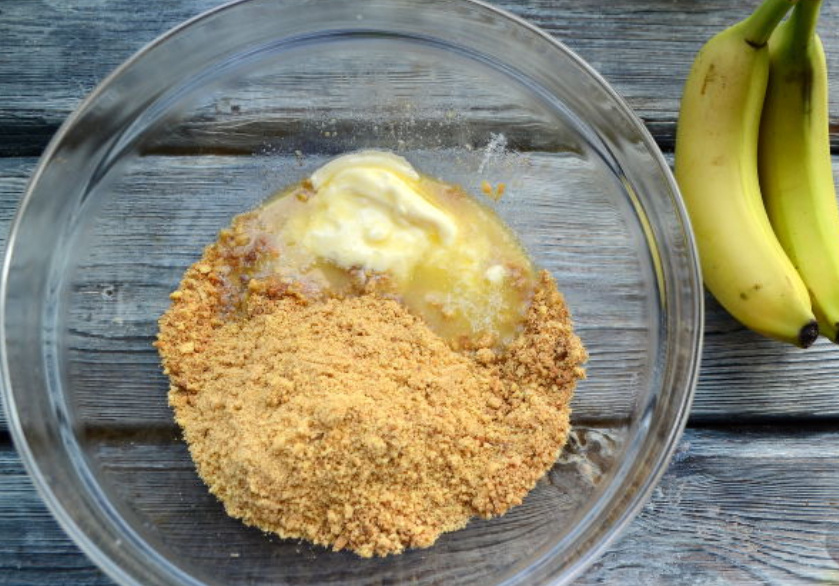 Песочное печенье измельчите скалкой или блендером. Влейте в крошки растопленное сливочное масло, перемешайте.