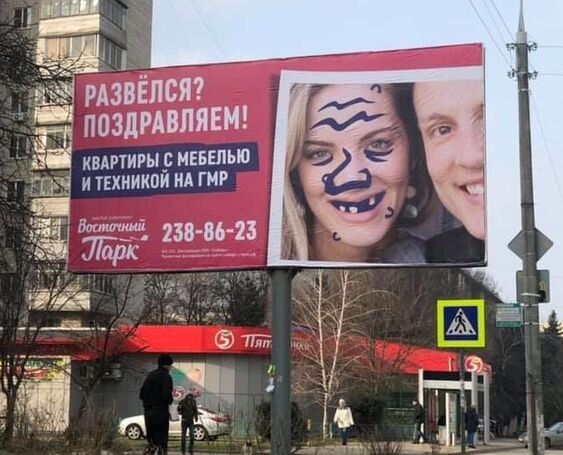 Рекламный щит с изображением испорченного фото пары и надписью "Развёлся? Поздравляем!" предлагает квартиры с мебелью и техникой, что вызывает неоднозначные эмоции и критику из-за неуместного юмора. 