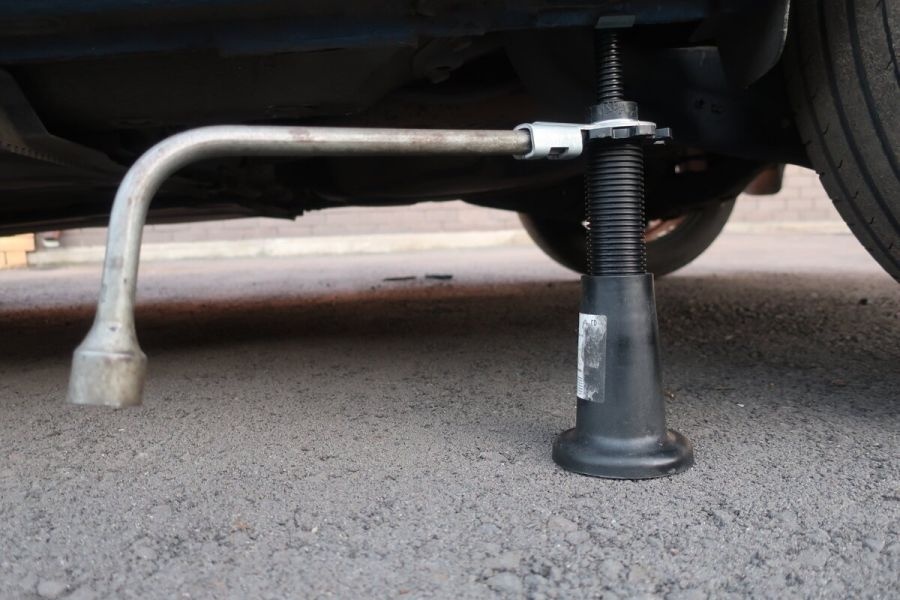 Машину помещают на ровное основание и устанавливают противооткатные башмаки. Затем заднюю часть приподнимают при помощи домкрата.
