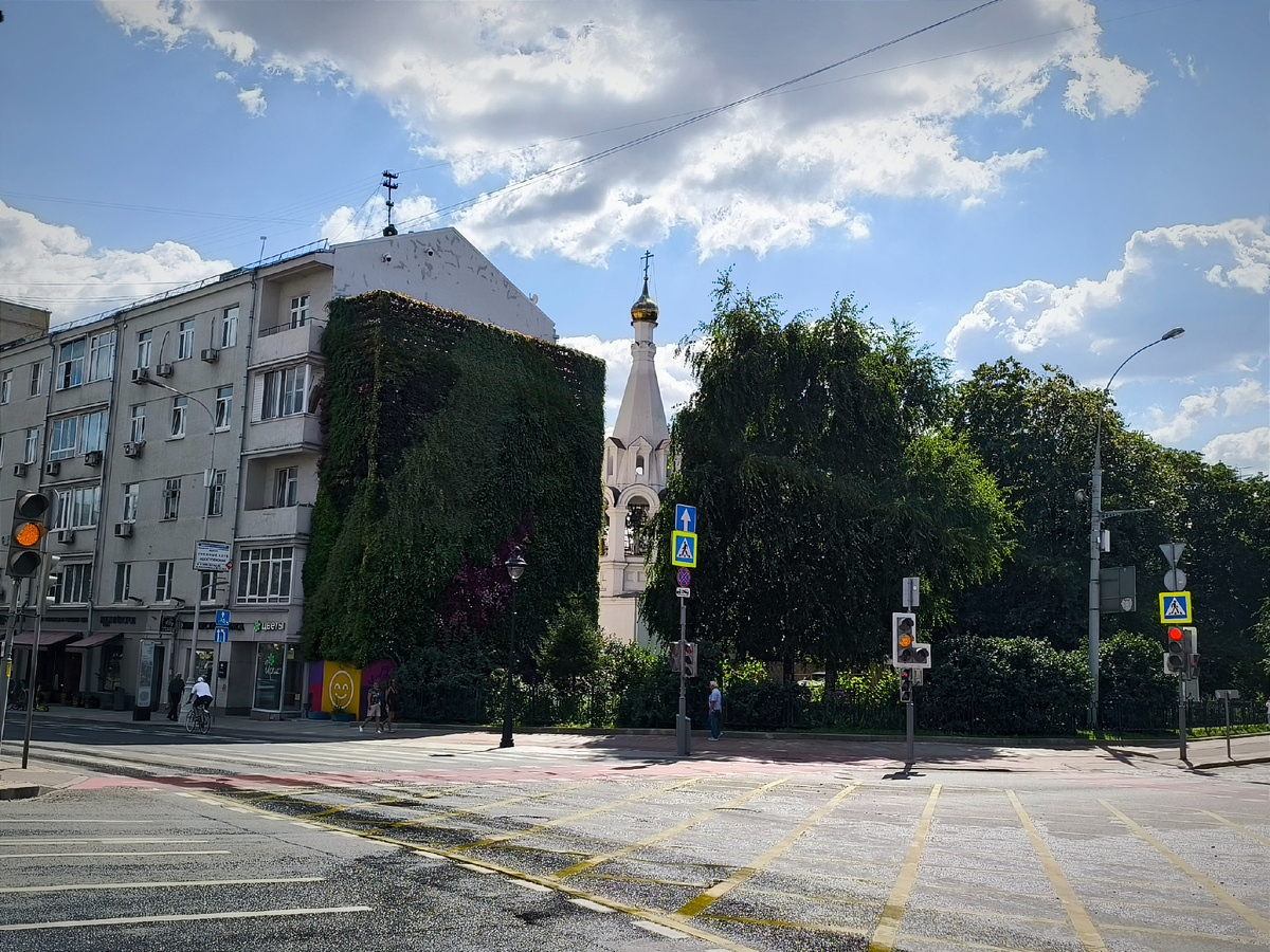 Колокольня храма виднеется в проёме зелёной стены.