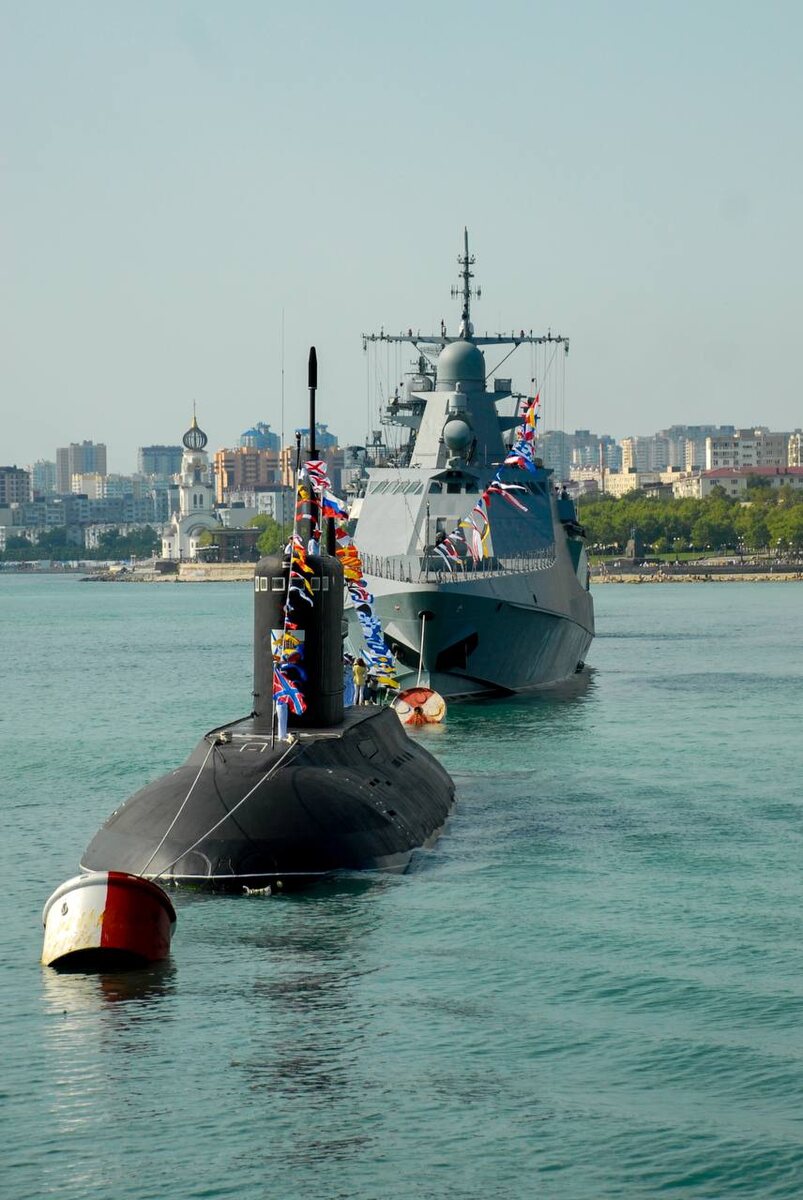 Тифлокомментарий. В цемесской бухте один за одним стоят подводная лодка и военный корабль. Они украшены разтяжками с флажками. 