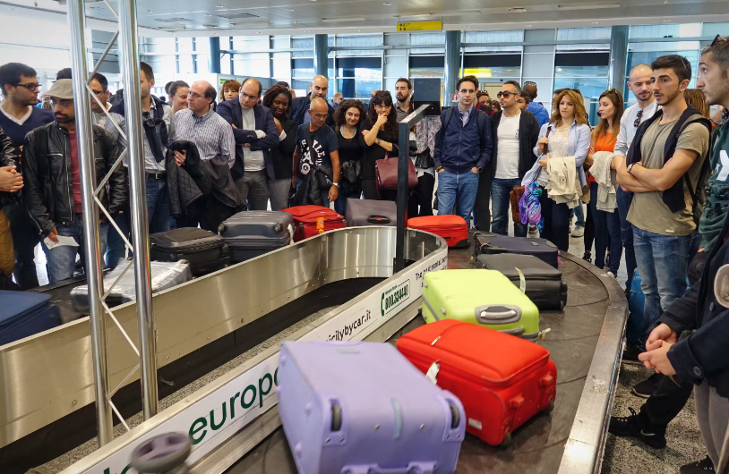 Пассажиры стоят вокруг багажной ленты со множеством сумок. Фото: MikeDotta 
