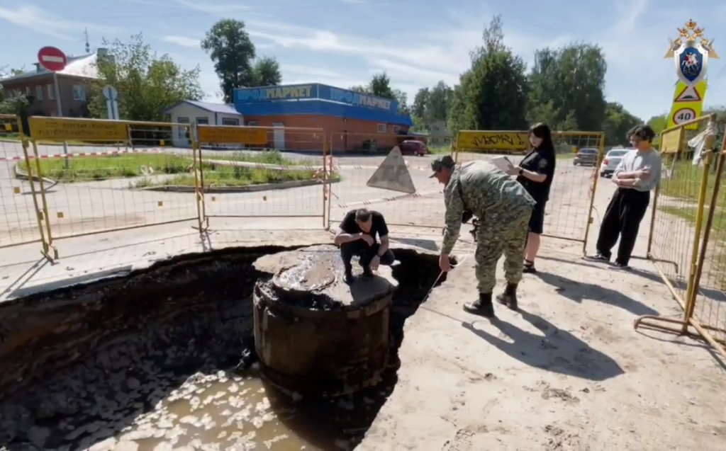 Следователи над осушенной ямой, образовавшейся в результате провала асфальта под воздействием кипятка