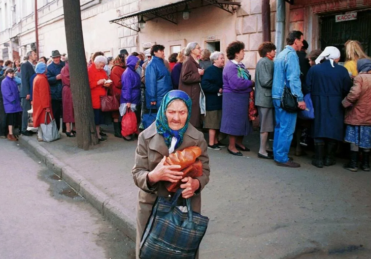                                                      «Очередь»

Холодное осеннее утро. Алексей, толком не проснувшись, одевался. Так ему казалось, одевала его мама. Женщина с усталым лицом и выделяющейся из причёски седой прядью волос. Они торопились. 
– Нужно успеть сынок. – Сказала мама Алексея. 
Алексей надел шапку и вышел в подъезд, следом вышла мать. Они спустились по лестнице на первый этаж. Вышли из подъезда и холод осени окутал их. Холодно и свежо, листья на деревьях, почти все опали. Мать заметно торопилась.  Алексей не поспевал за ней, но крепко держал маму за руку, чтобы не отстать. Время было около шести утра. Они подходили к жилому зданию. На первых этажах  жилого пятиэтажного дома, располагался единственный магазин, на весь район. Работать магазин начинал с девяти утра. Возле магазина уже была большая очередь, человек шестьдесят.  Люди,  поёжившись от холода,  нервничали. Кто-то с кем-то спорил или ругался в толпе.
– Тише товарищи, давайте соблюдать дистанцию, не ссорьтесь, все согласно очереди! – Алексей узнал голос отчима. Высокий, крепкий мужчина в пальто, с длинными рыжими усами, колючим взглядом и белым шарфом на шее.
– Светлана, мы двадцать вторые в очереди, вот за этой женщиной, её Лидия Михайловна зовут.
– Доброе утро, меня зовут Светлана. – Поздоровалась мать с женщиной.
– Я на работу, вот деньги и карточки. – Сказал отчим, обнял маму и исчез в толпе. Народ прибывал. Алексей отходил от толпы на пару метров и понимал, что очередь растёт. И действительно было видно со стороны, что людей уже намного больше, чем было. Около ста человек, стояли и ждали, когда откроется магазин, чтобы в порядке очереди, на талоны, дающие право приобрести в ограниченном количестве, необходимые продукты питания. Когда очередь приобрела большое и длинное очертание, Алексей уже не отходил от матери, держал ее за руку и думал.
«Вот если бы я жил в другой стране, может быть, и не надо было стоять за продуктами, по три часа?» – Посетила грустная мысль  мальчика.
Его мама тоже была в своих мыслях и постоянно смотрела вдаль.
« Господи» –  Летели мысли в голове матери Алексея.
«Как так вышло,  вроде живём в современном обществе, нет войны, победили практически все болезни, а жить по-человечески не можем. Рушился коммунистический строй, разваливалась самая великая и большая страна на планете, кто бы мог подумать или предугадать такое...
Мы первые побывали тридцать лет назад в космосе, сейчас не можем прокормить семьи...»
– Эти мысли не давали покоя Светлане. Она посмотрела на сына, как ей показалось, он стоял и засыпал на ходу.
– Бедный ребёнок. – Проговорила она вслух и прижала его рукой крепче к себе. Алексей немного замёрз, но не спал, просто закрыл глаза и прижался к матери. Ему казалось все происходящее, каким то не реальным и не правдоподобным.  Он хотел домой, точнее, хотел в другой мир, где всё будет хорошо и мама будет чаще весёлой, где отчим не будет сутками пропадать на работе, а будет с ним ходить на рыбалку и смотреть мультфильмы. Ему очень хотелось туда, где всё будет, по-другому.  Но, где эта страна или мир он не знал. А самое главное, маленький ребёнок не знал, как туда попасть...
После трёх  часов ожидания, толпа оживилась. Время подходило к открытию магазина. Люди в очереди общались о своих житейских заботах  или обсуждали происходящее в стране, которая не могла быть прежней, а какой быть новой ещё не знала…
Открылась дверь. Из неё вышел заведующий магазином.
– Товарищи, прошу минуту внимания! – Заведующий магазином сорванным голосом, пытался успокоить всколыхнувшуюся толпу, сначала назад при открытии двери, а потом  вперёд.
– Товарищи, сегодня завоза хлеба и сахара не будет! Есть макароны, пшено,  водка и чай! Всё в ограниченном количестве! – Толпа озверела от такой новости, что сахара и хлеба нет сегодня. Послышались возгласы, недовольных, ожидающих людей.
– Когда же этот бардак  кончится! Как в блокаду по карточкам стоим, по пять часов в очереди и не можем купить хлеб! – Голос звучал,  как гром и был слышен особенно чётко из других недовольных выкриков в очереди. Женщина преклонных лет, возмущалась больше всех и негодовала. Но это всеобщее негодование быстро прошло, очередь тронулась с места. Людей начали впускать в магазин по пятнадцать человек, чтоб не допустить давки в зале. Через десять минут начали выходить первые, счастливые и довольные покупатели с авоськами и бумажными кулями. Этот день прошел без массовой давки. Слава богу, ни кто не пострадал в очереди…
Это время Алексей запомнит, на всю оставшуюся жизнь. Он, вырос и живёт в другой стране, как и мечтал,  где жить стало намного лучше.  Когда он стал взрослым и у самого появились дети, он старался не рассказывать о своём детстве. Его дети, жили хорошо и слово дефицит и очередь им были не знакомы. Страна снова вставала с колен. Обретала вновь единство и благополучие для многострадального русского народа, после нищеты и разрухи. А про очереди за продуктами и нищету тех времён Алексей старался не  говорить при детях. Иногда по вечерам, засыпая из своей спальни, дети слышали, как на кухне папа и мама вспоминали о своём детстве. Уверенные, что их дети спят.

Погасло пламя, рухнул строй.
Пропала правда, цель, покой.

Редакция 2024 года. Изменения будут внесены в декабре 2024 года в сборник рассказов "Шум за дверью тишины" первое издание.