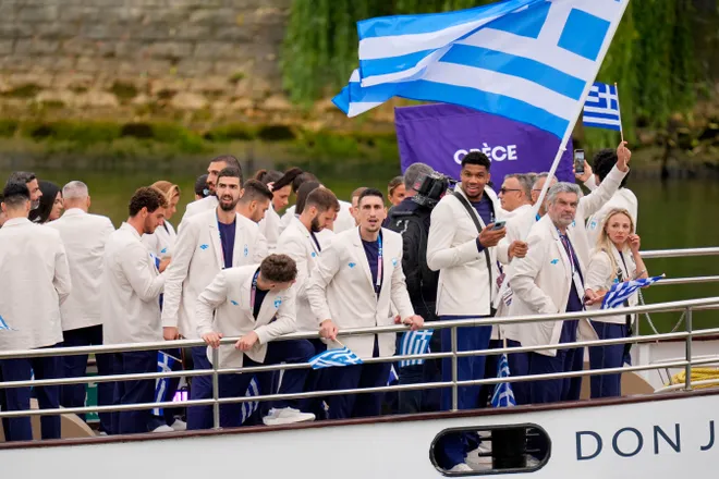 Яннис Адетокунбо держит греческий флаг, когда их лодка проплывает мимо во время церемонии открытия летних Олимпийских игр 2024 года в Париже. Эндрю Неллес, USA TODAY Sports