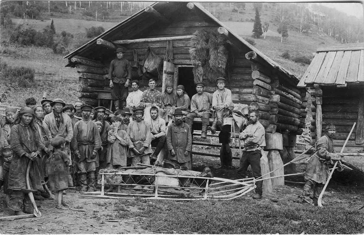 Группа шорцев из улуса Кумыс. На переднем плане охотник на лыжах с нартой за спиной демонстрирует снаряжение для зимней охоты экспедиции. Фото 1913 года