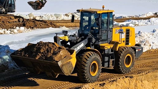 An excavator loads sand into a bucket for a loader.