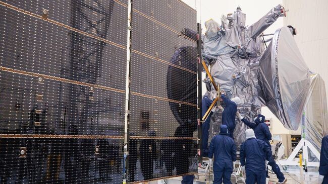     Технические специалисты прикрепляют солнечные батареи из пяти панелей к космическому аппарату NASA Europa Clipper внутри Центра обслуживания опасных грузов в Космическом центре имени Кеннеди во Флориде 2 августа 2024 года.    
 Источник: NASA / Kim Shiflett