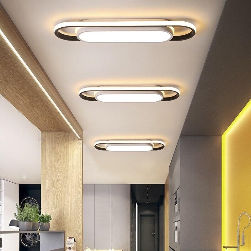 Современный потолочный светильник с элегантным дизайном, сочетающий в себе гладкие металлические элементы и мягкое, теплое освещение. Светильник подвешен к потолку в стиле минимализма и отбрасывает мягкие тени на современную гостиную со стенами нейтральных тонов и стильной мебелью, подчеркивая уютную атмосферу.